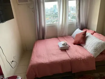 a small bedroom with a pink bed with a window at pierrecondotel in Manila