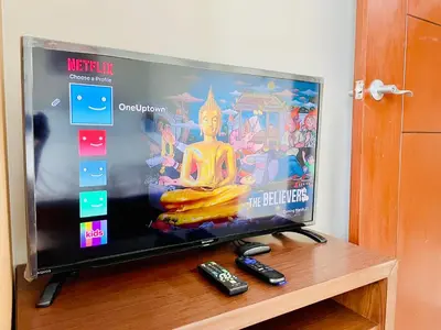 a flat screen tv sitting on a table with two remote controls at 1 Queen Bed & 2 double beds at One Uptown Residences with XBOX and Netflix in Manila