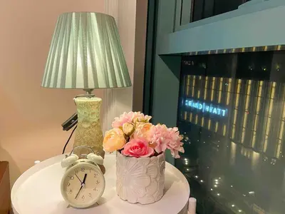 a table with a lamp and a clock and flowers at Bgc 1br Condo Across Uptown Mall, Hyatt #oursw7b2 in Manila