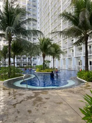 a swimming pool in front of a building with palm trees at D'Shore to Relax Shore Residences MOA PASAY in Manila