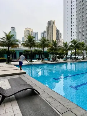 a person standing next to a large swimming pool in a city at Serene Suite In Jazz Residences in Manila