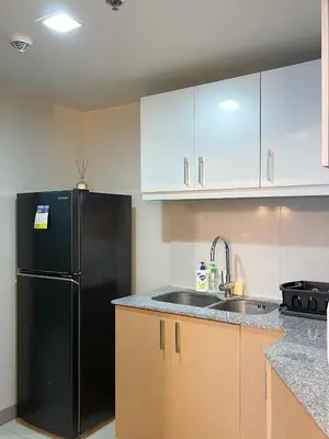 a kitchen with a black refrigerator and wooden cabinets at BGC 3BR Uptown Parksuites with bathtub 16 in Manila