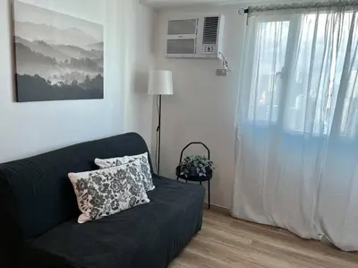 a living room with a black couch and a window at Modern 2BR in Central Makati! Netflix Wi-Fi Pool in Manila