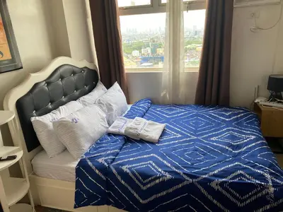 a bed with a blue and white comforter and a window at Pierrecondotel in Manila