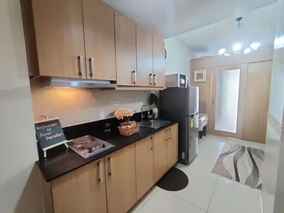 a kitchen with wooden cabinets and a black refrigerator at Shell Residences Condo Suite Staycation near MOA and Airport in Manila