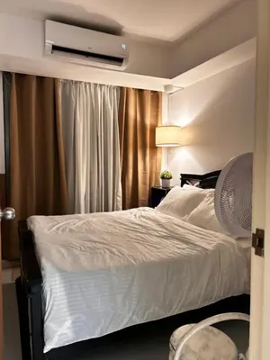 a bedroom with a white bed and a fan at Caroshiro Staycation Azure Uban Resort in Manila
