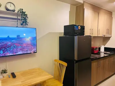 a kitchen with a black refrigerator and a tv on the wall at 1BR Condotel with Balcony at FAME Residences #FM27 in Manila