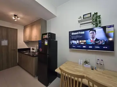 a kitchen with a black refrigerator and a tv on the wall at 1BR Condotel with Balcony at FAME Residences #FM29 in Manila