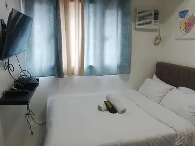 a bedroom with a bed and a television and a window at Grand Riviera suite Condotel Near SLEC in Manila