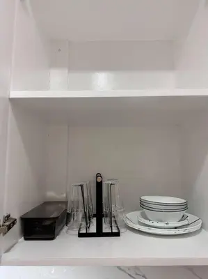 a white shelf with plates and dishes on it at Cozy Condo in Taguig in Manila