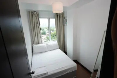a small room with a window with white sheets and pillows at Hayahay Rentals in Manila