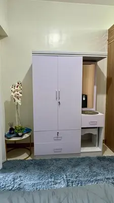 a large white cabinet in a bedroom with a table at The GoodVibes Condotel Red Residences Makati in Manila