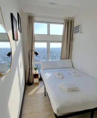 a white bed in a room with a large window at Cozy 1 BR San Lorenzo Place Netflix 4KM NAIA in Manila