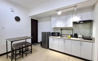 a kitchen with white cabinets and a table and a refrigerator at Cozy 1 BR San Lorenzo Place Netflix 4KM NAIA in Manila