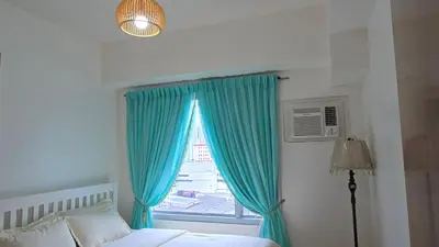 a bedroom with a bed and a window with blue curtains at 8 Adriatico Condotel Unit Facing Manila Bay in Manila