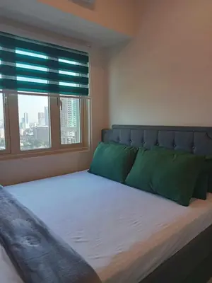 a bedroom with a bed with green pillows and a window at The Prestige Bayview with Balcony in Manila