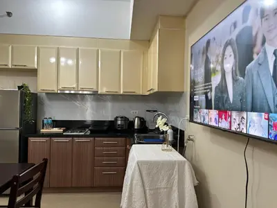 a kitchen with a table and a tv on the wall at COZI Venice Luxury Residences Alessandro BGC w Pool Gym in Manila