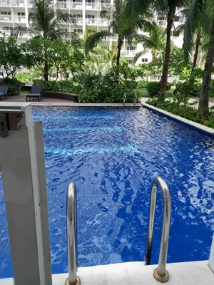 a large blue swimming pool with palm trees and a building at Shore Residence Direct Pool Access MOA Complex in Manila