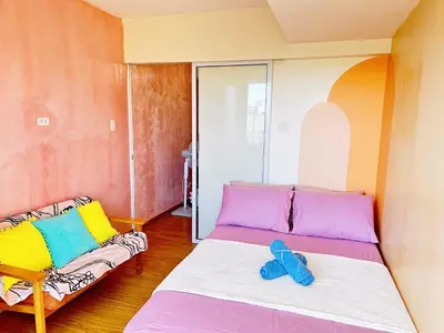 a bedroom with a bed with colorful pillows and a couch at 2 Bedroom Summer Themed Unit at Azure in Manila