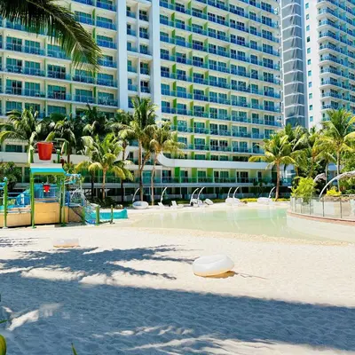 a playground in front of a large building with palm trees at 2 Bedroom Summer Themed Unit at Azure in Manila