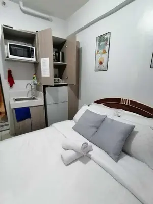 a small bedroom with a white bed and a sink at Dens condotel Metro Manila in Manila