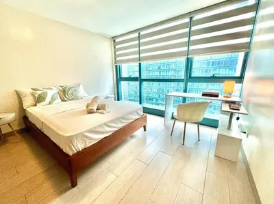a bedroom with a bed and a desk and a window at Cozi Uptown 1br suite Mitsukoshi Mall BGC in Manila