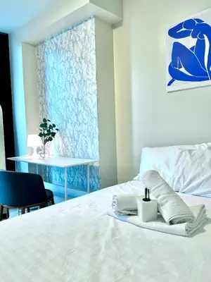 a bedroom with a white bed with a chair and a table at Cozi 1br suite Grand Hyatt BGC wifi pool in Manila