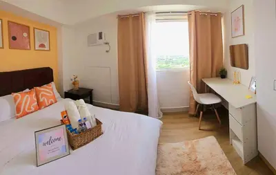a bedroom with a white bed and a desk and a window at Bigg Apol Suite in Manila
