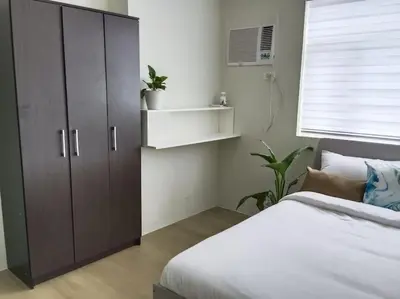 a bedroom with a bed and a cabinet and a window at Vista GL Taft Studio Unit in Manila