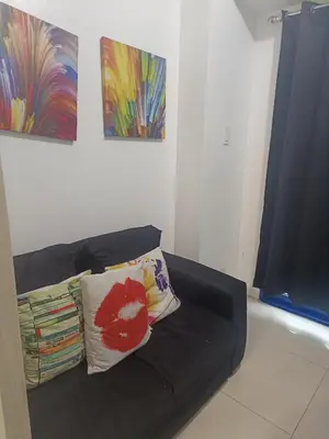 a black couch with two pillows in a room with paintings at SEA RESIDENCES NEAR MALL OF ASIA BY Amigo's place in Manila