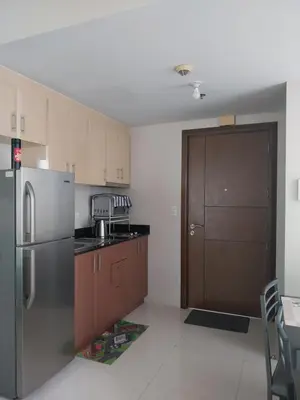 a kitchen with a stainless steel refrigerator and wooden cabinets at Emy Cozy Studio unit with street view balcony in Manila