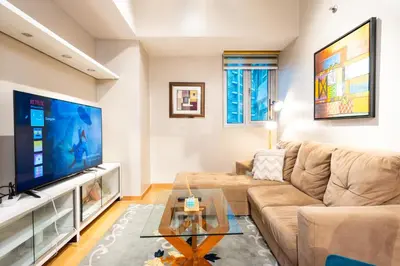 a living room with a couch and a large tv at Avant at the Fort BGC 1BR Flr to Ceiling Cor Unit with Great View in Manila