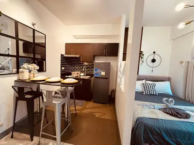 a small room with a bed and a kitchen with a table at Your perfect retreat in Stamford! Enjoy our stylish, fully furnished studio just steps away from the vibrant Venice Mall in Manila