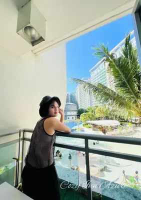 a woman standing on a balcony looking out at the beach at Cozy Inn Azure in Manila