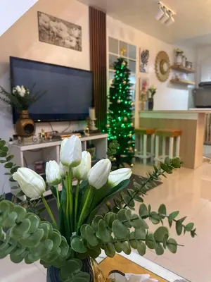 a vase with white flowers in a living room with a christmas tree at Elyana's Staycation in Pasalada