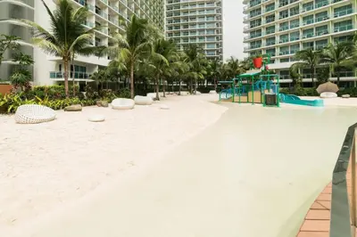 a playground on a beach with palm trees and buildings at 1BR Condotel at Azure Urban Resort Near Airport #AZ05 in Manila