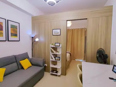 a living room with a gray couch and a yellow pillow at 1BR Condotel with Balcony at FAME Residences #FM36 in Manila