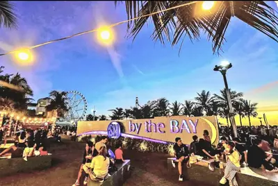 people sitting on benches in front of a sign that reads by the bay at Near MOA Manila Bay Airport via NAIAX Balcony-Pool View WiFi SHELL Residences in Manila