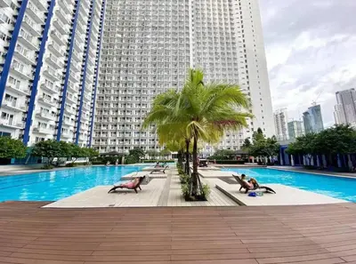 a swimming pool with palm trees and a large building at Cozy Makati Condo Getaway with balcony in Manila