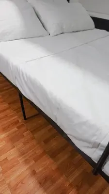 a bed with white sheets on a wooden floor at Modern Condo for 6, with Kitchen, Wi-Fi & Netflix, Near MRT Boni in Manila