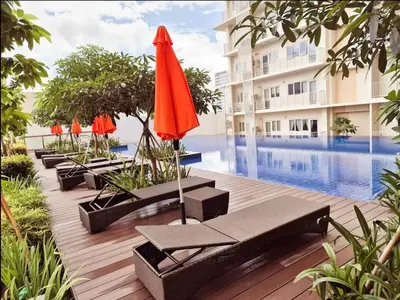 a pool with chairs and umbrellas next to a building at 10G Cozy Condo at Park McKinley West near Venice Mall in Manila