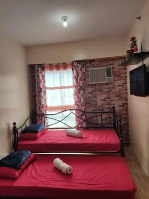 a bedroom with two beds with red sheets and a window at Near Manila Airport COZY Studio Condo With Kitchen 11P in Manila