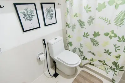 a bathroom with a toilet and some pictures on the wall at Excellent Location 2 BDRM Homey Wifi Near Airport in Manila