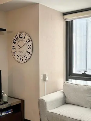 a clock on a wall next to a chair and a window at Deluxe Studio with Balcony at Greenbelt Makati Manila in Manila