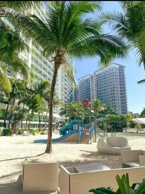 a playground on the beach with palm trees and buildings at DT SUITES AND RESORTS at Azure Paranaque in Manila