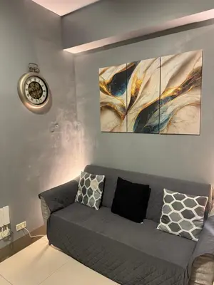 a living room with a gray couch and a clock at Fame Residences Mandaluyong 1 BR with two Big TV with Balcony in Manila