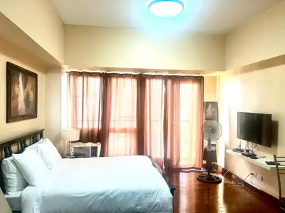 a bedroom with a white bed and a television at 20C Staycation away from home in Manila