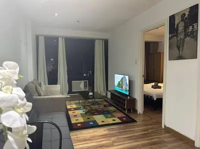 a living room with a couch and a tv in a room at Spacious Corner 1 Bedroom with Balcony Gramercy in Manila