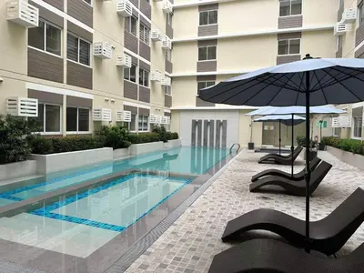 a swimming pool with chairs and an umbrella next to a building at El Suite in Puting Kahoy