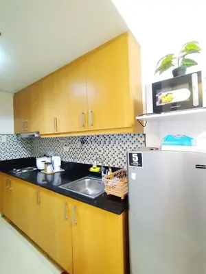 a kitchen with wooden cabinets and a white refrigerator at Comfystay at Shell Residences in Manila